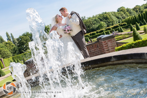 Romantisches Brautpaar-Shooting am Brunnen mit sprudelnder Fontäne – das Paar posiert vor der beeindruckenden Wasserfontäne in einer eleganten und stimmungsvollen Szene.