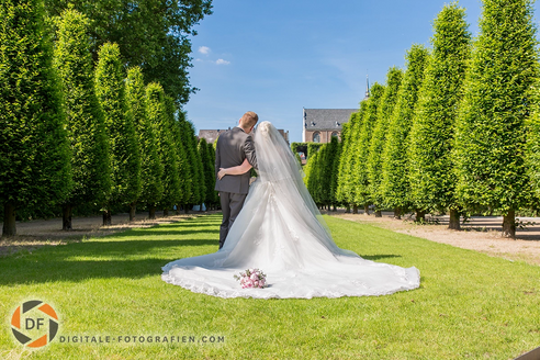 Brautpaar-Shooting im Park – die Braut steht mit dem Rücken zur Kamera und präsentiert ihr wunderschönes Brautkleid, während das Paar in einer idyllischen Parklandschaft posiert.